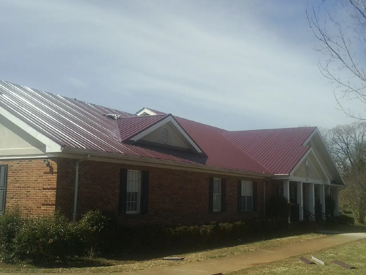 Red metal roof with gabled entries on a long brick building, from a Hail Damage Roof Repair job in Saint Edward