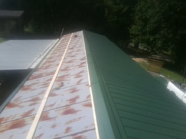 Old rusted panels beside newly installed green metal roofing — Wind Damage Roof Repair by Roofing Brothers in Saint Edward