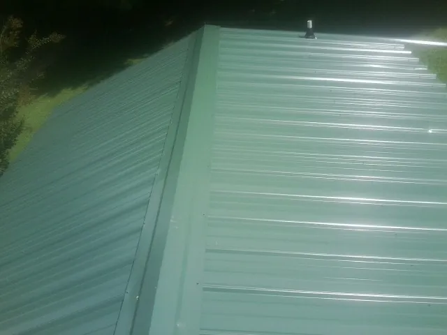 New green metal panels meeting at the ridge of a roof — Flat Roof Repair work by our crew in Saint Edward