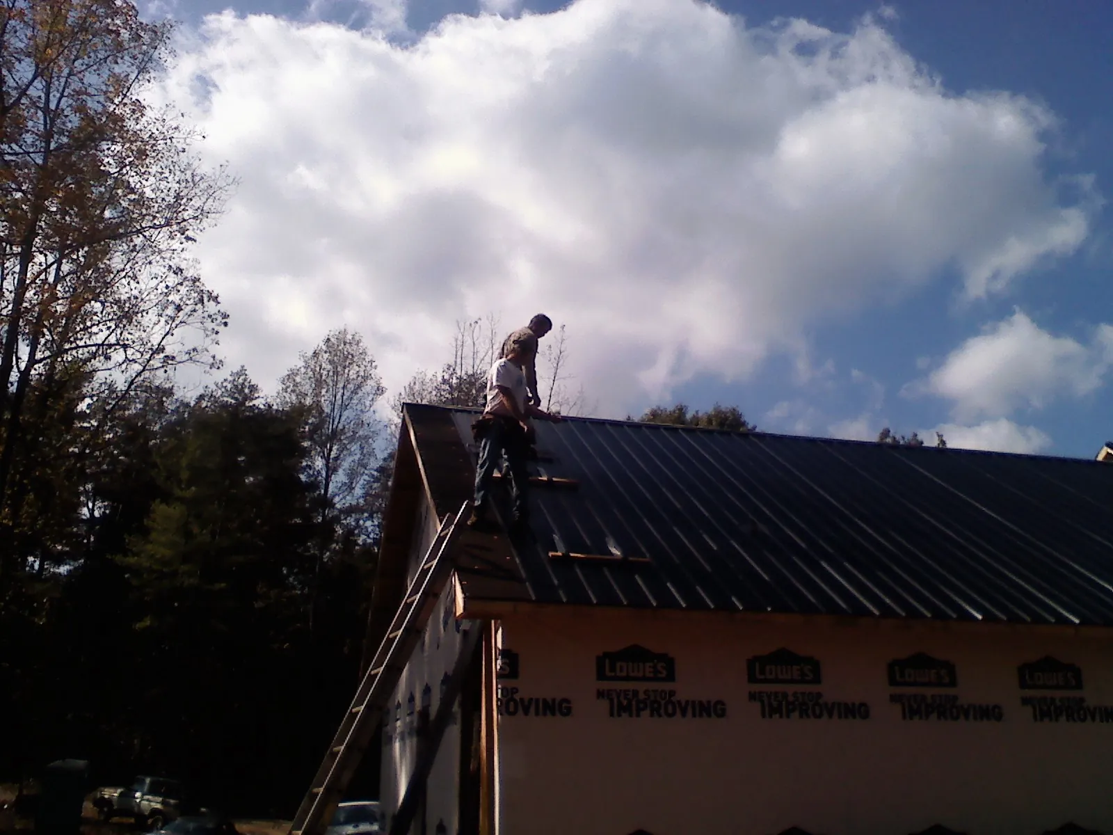 Roofer fastening dark metal panels high against a cloudy sky, from a Roof Inspection job in Saint Edward