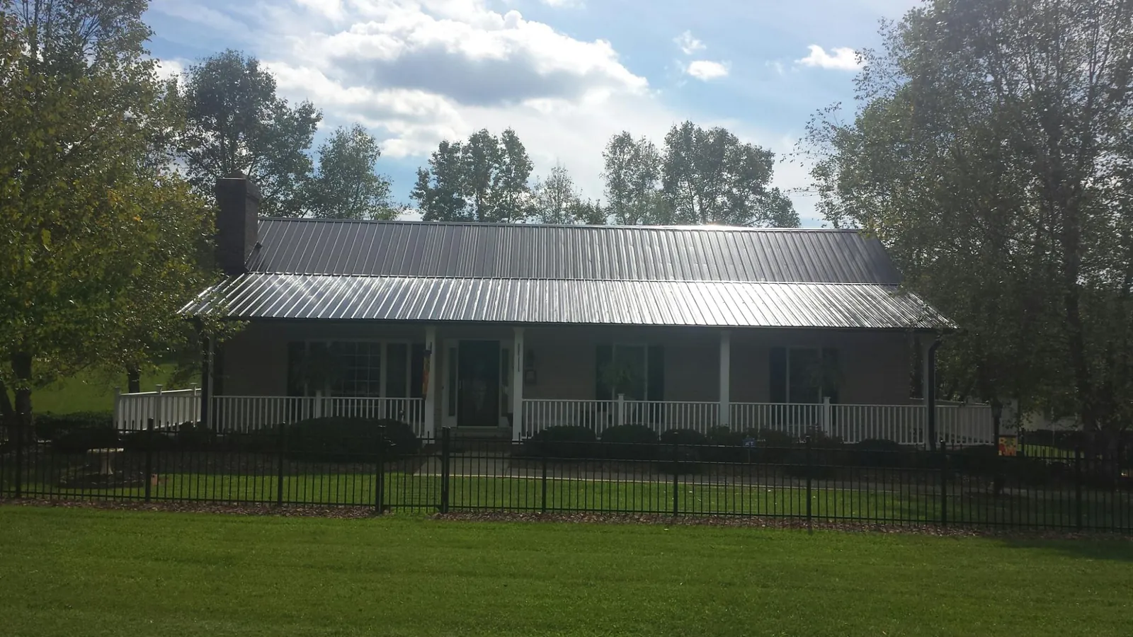 Gray metal roof on a brick ranch with a full width front porch — Gutter Guard Installation work by our crew in Saint Edward