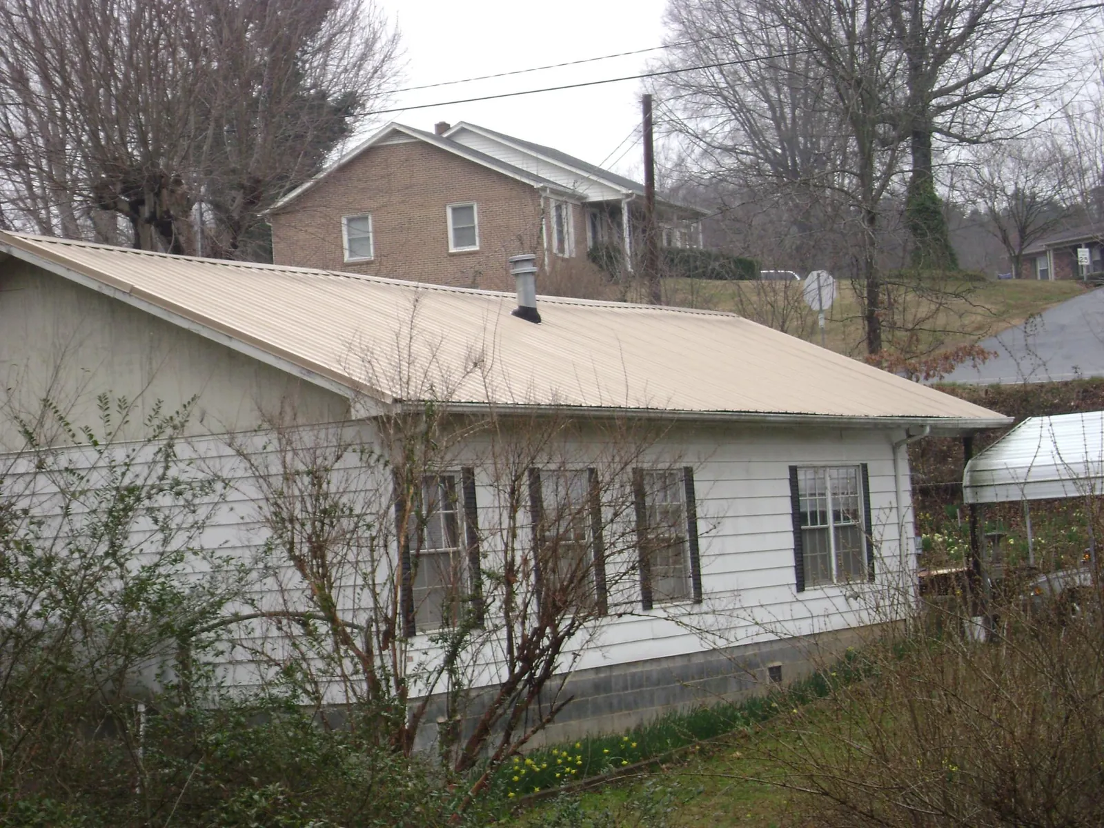 Tan metal roof on a white sided house set into a hillside — Commercial Roofing by Roofing Brothers in Saint Edward