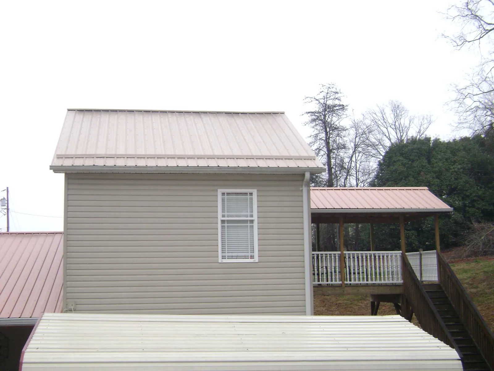 Tan metal roofs on a two story addition and attached porch, from a Roof Replacement job in Saint Edward